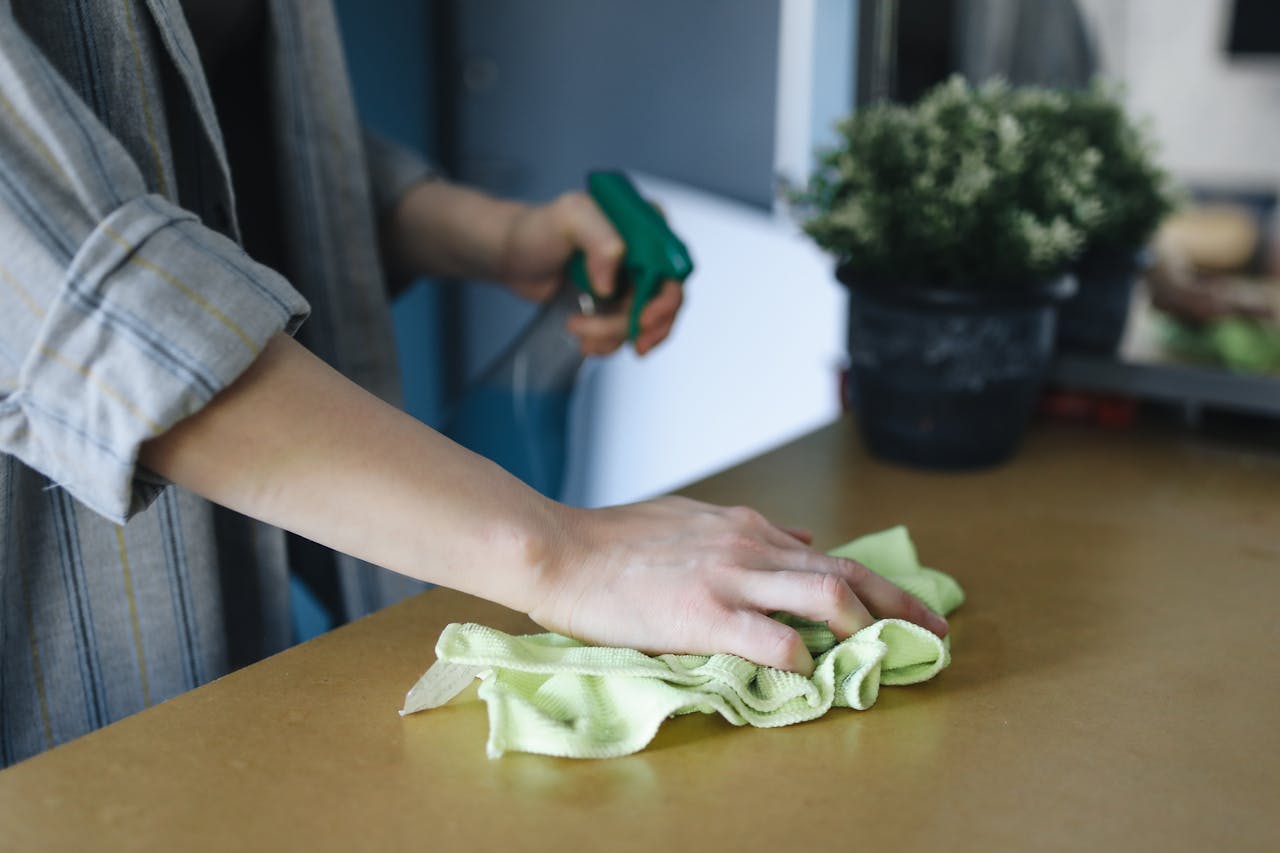 Close-up of a woman wiping a table with a spray bottle and cloth indoors, symbolizing effective housekeeping.