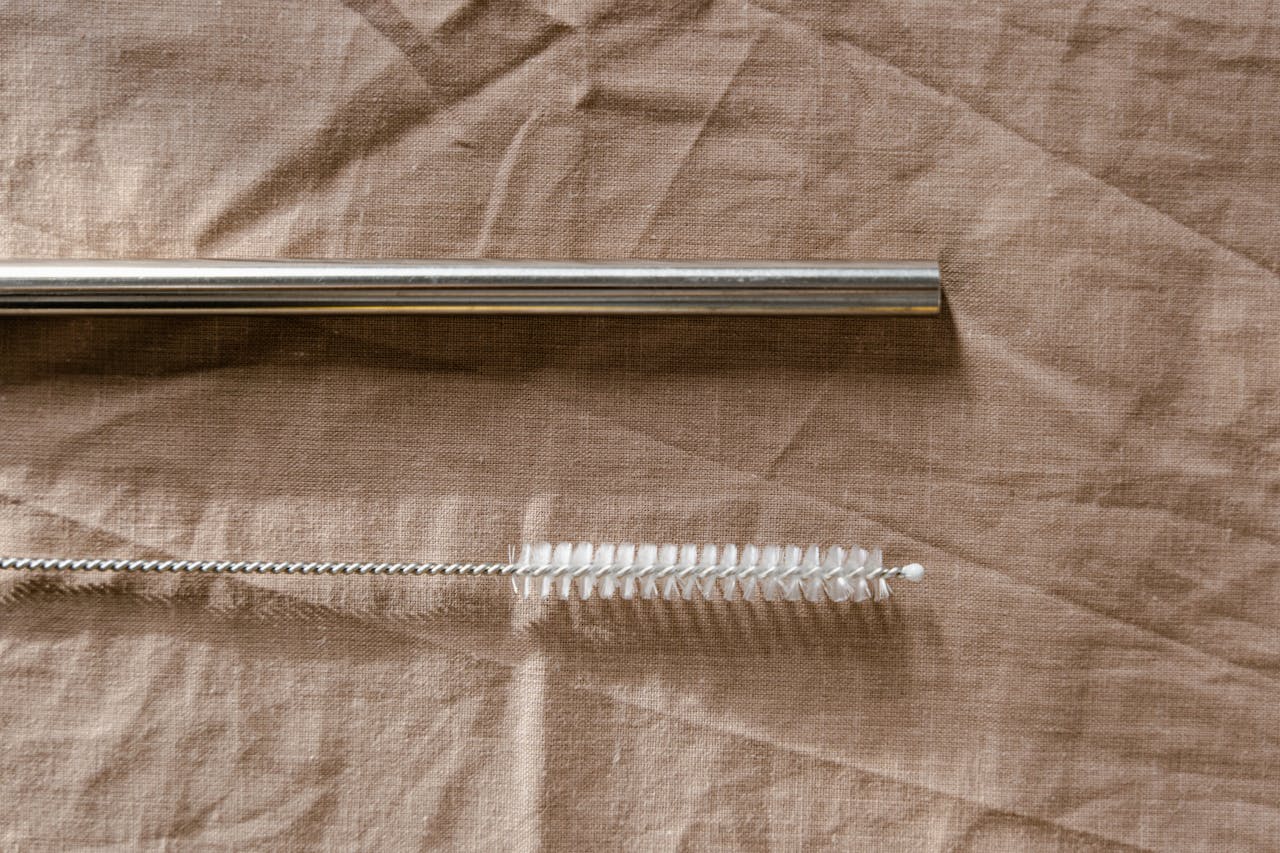 Eco-friendly metal straw and cleaning brush on a fabric background.