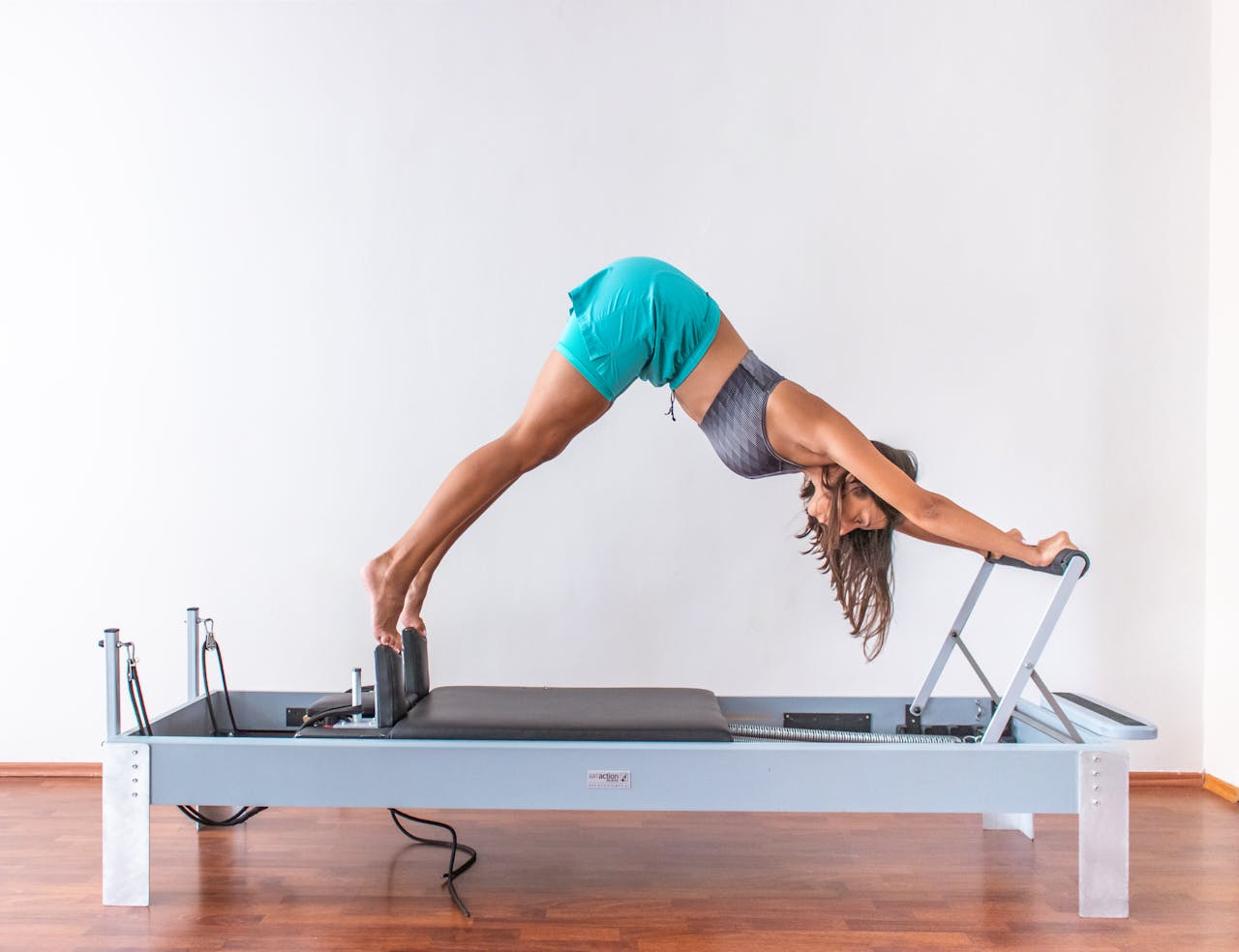 A woman performs a pilates exercise on a reformer, demonstrating flexibility and fitness indoors.