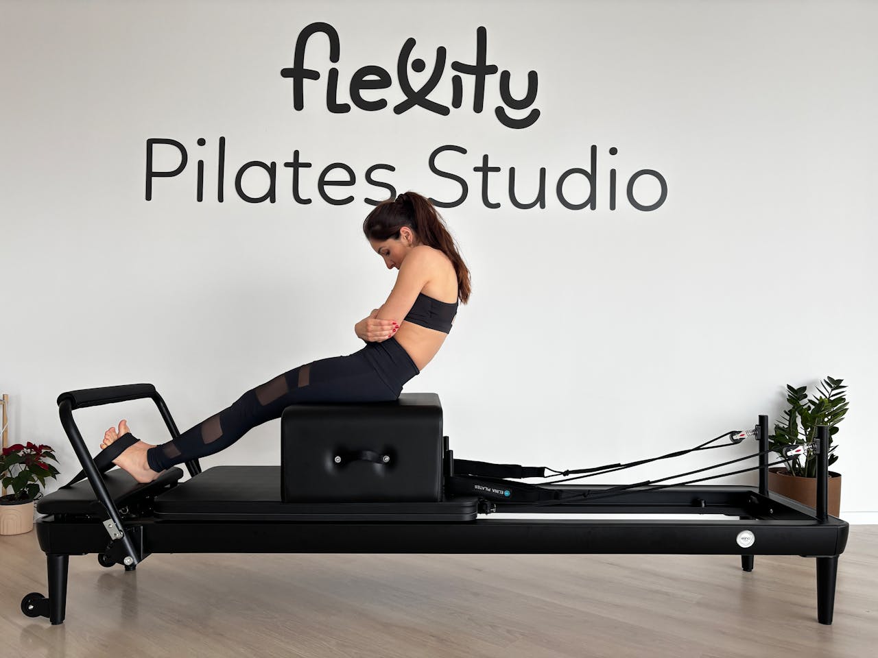 A woman is doing a Pilates workout on a reformer machine at a Pilates studio.